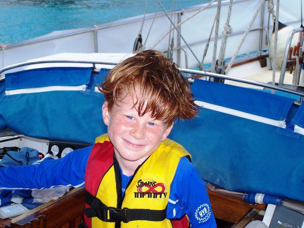 child with freckles smiling wearing life jacket on boat