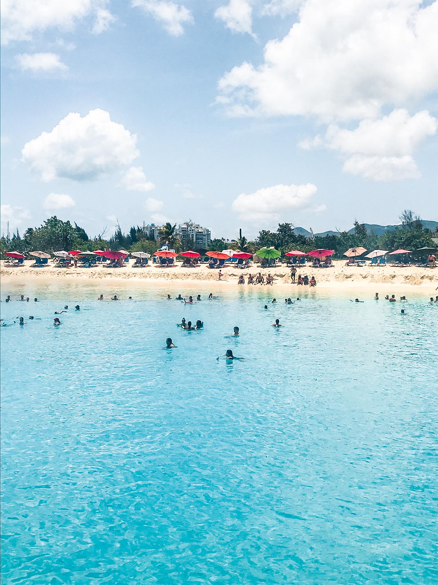 people swimming in water at beach with umbrellas on beach