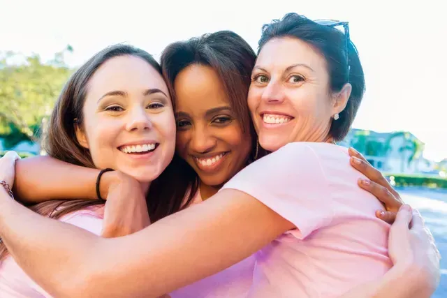 Three smiling people in pink shirts embrace outdoors. Three smiling people in pink shirts embrace outdoors.