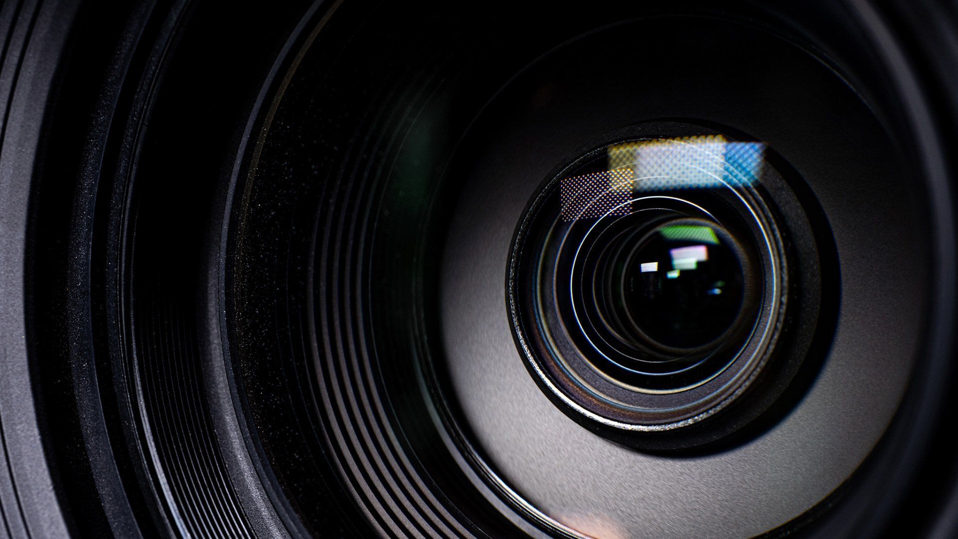 Close-up of a camera lens, with multiple reflective surfaces and a dark, ribbed outer casing.