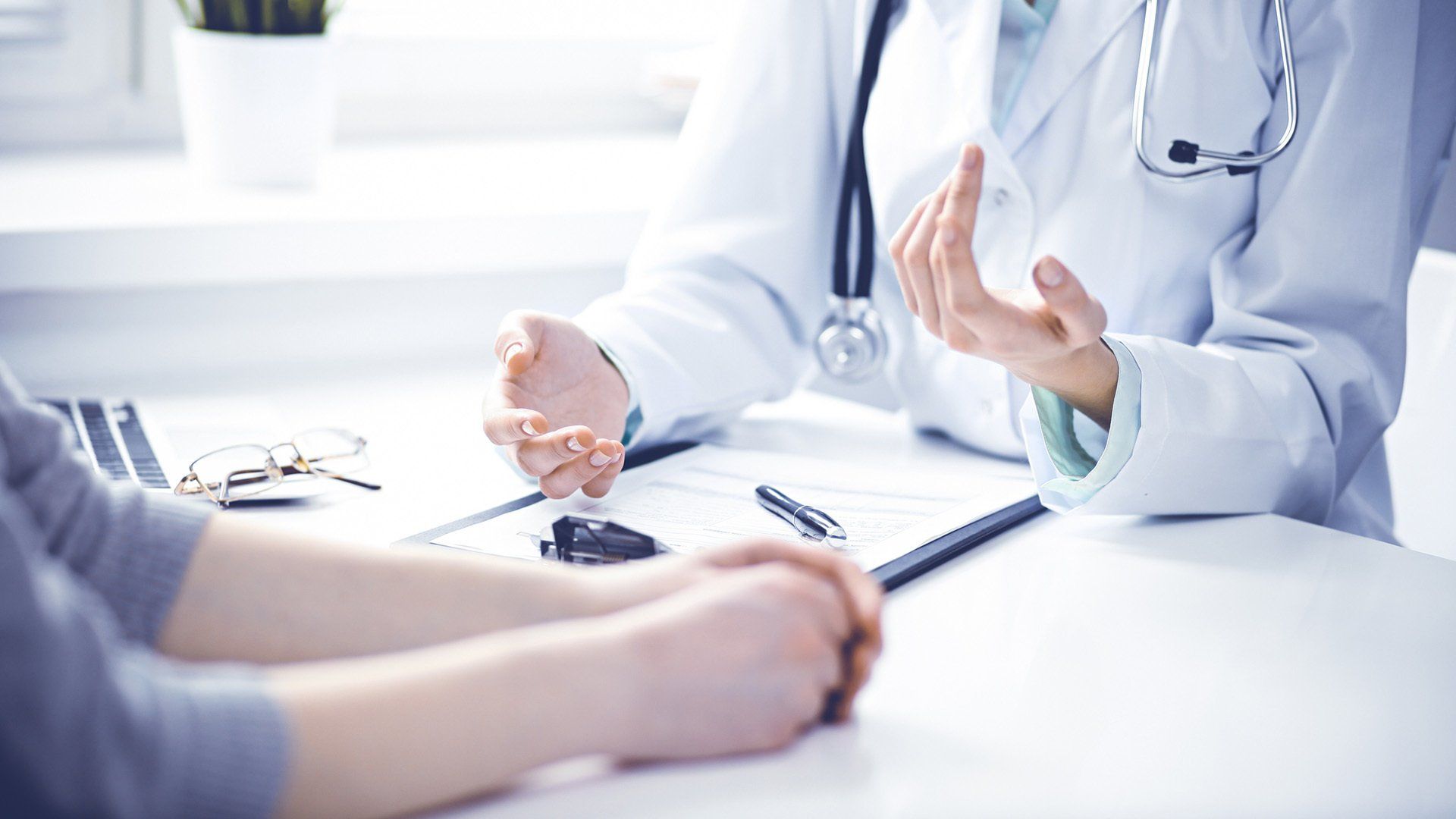 Doctor in white coat gesturing to patient in a consultation room.