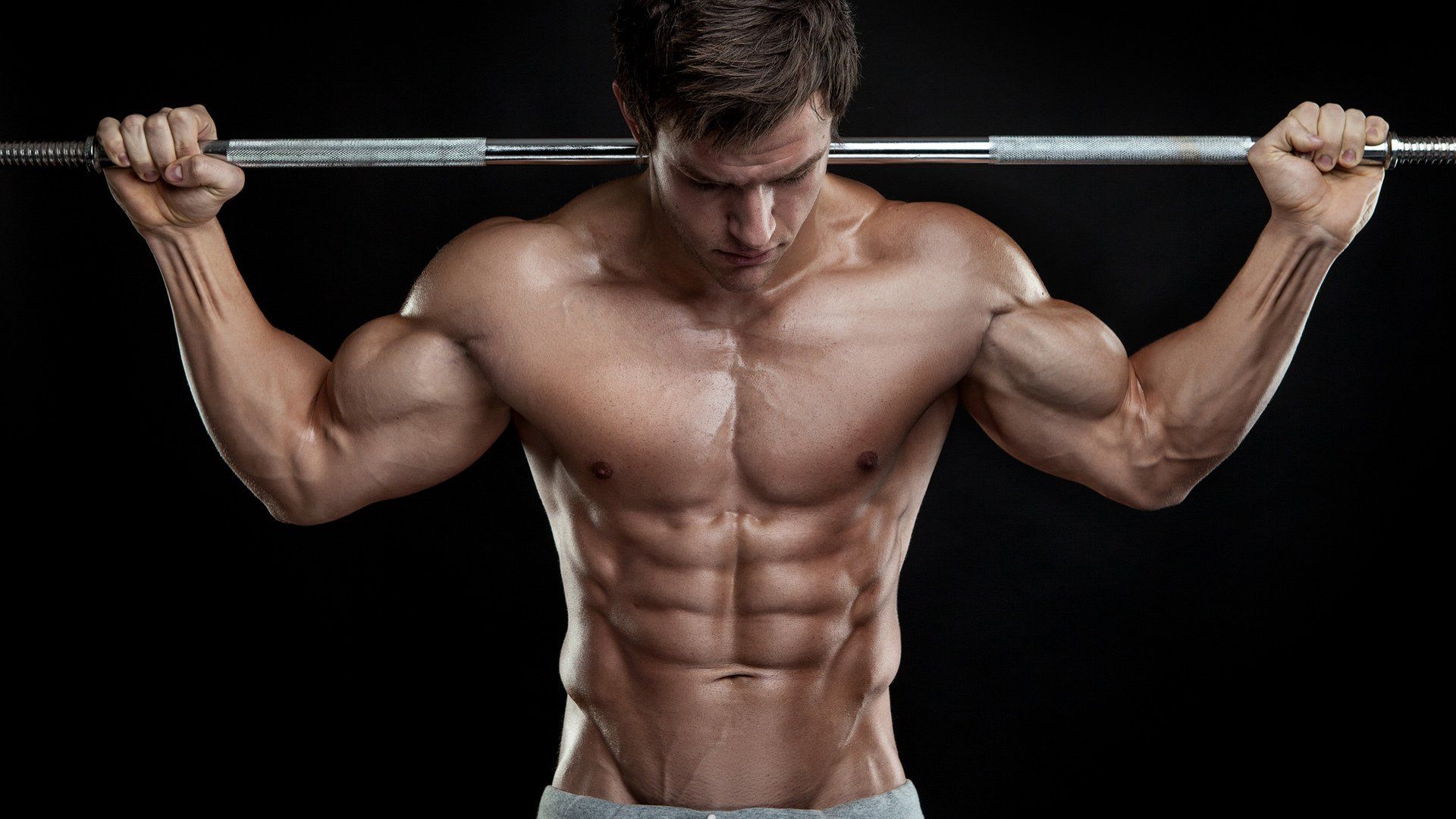 Muscular person with barbell on shoulders, sweating, black background.