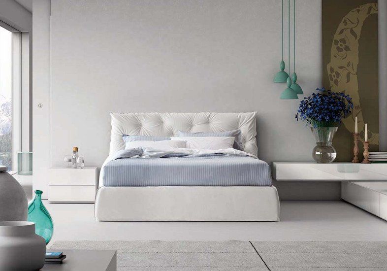 una camera con un letto bianco con la testata imbottita  e dei comodini a muro