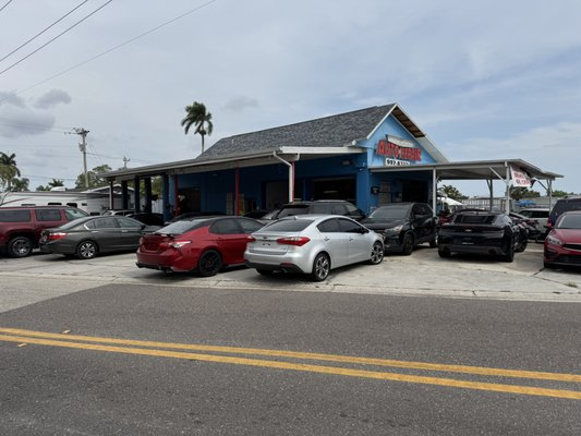 A blue restaurant building with a gray roof, surrounded by various cars parked in front under a covered patio area.
