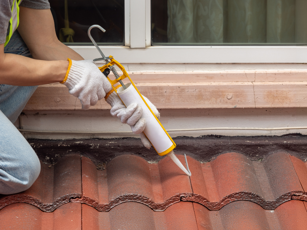 A man is applying sealant to a tiled roof.