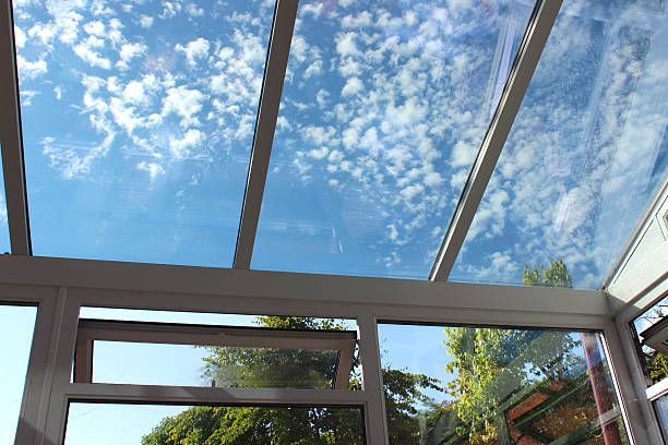 A conservatory with a glass roof and a blue sky behind it.