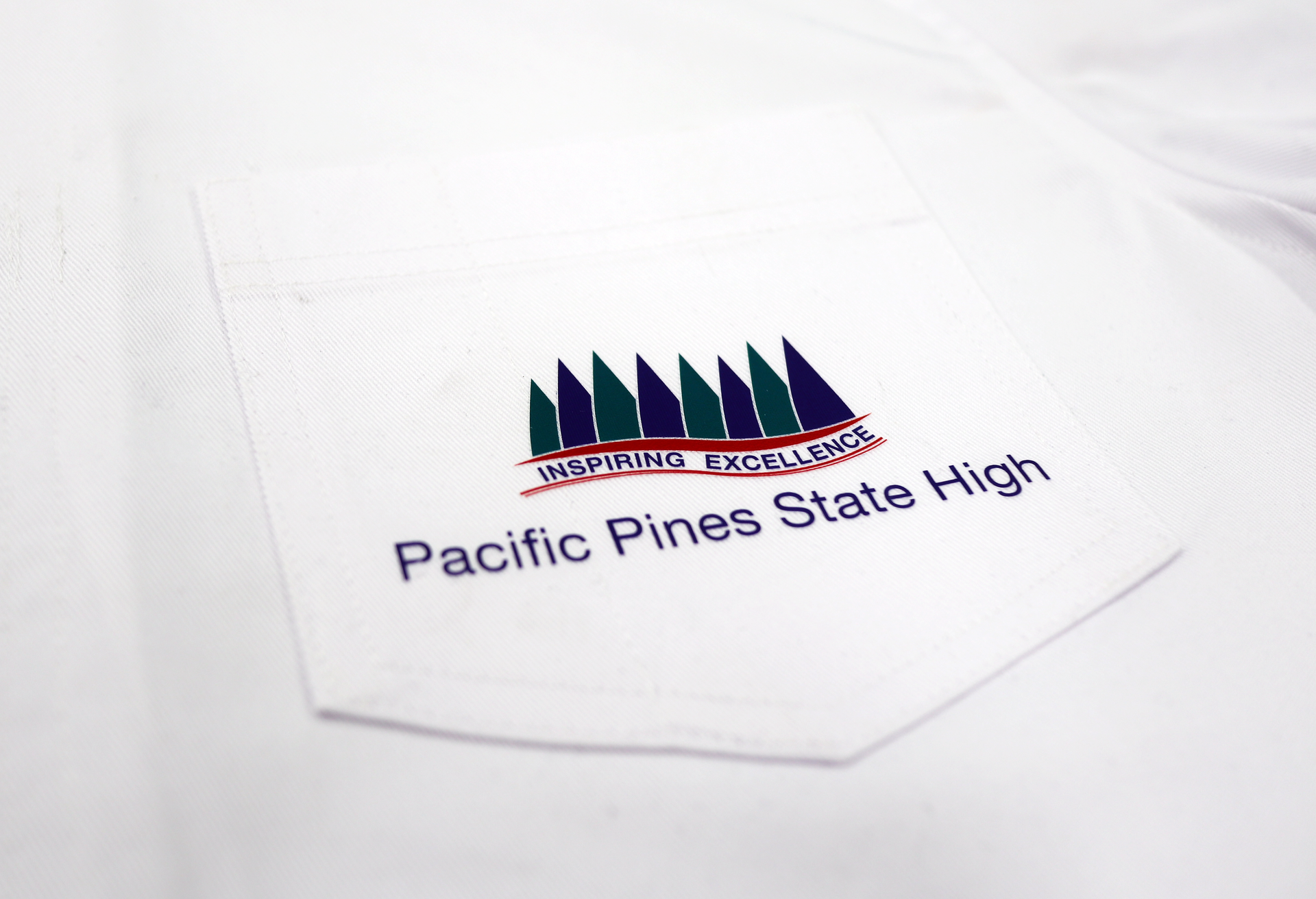 White lab coat pocket with printed school logo: green pine trees, maroon wave, 