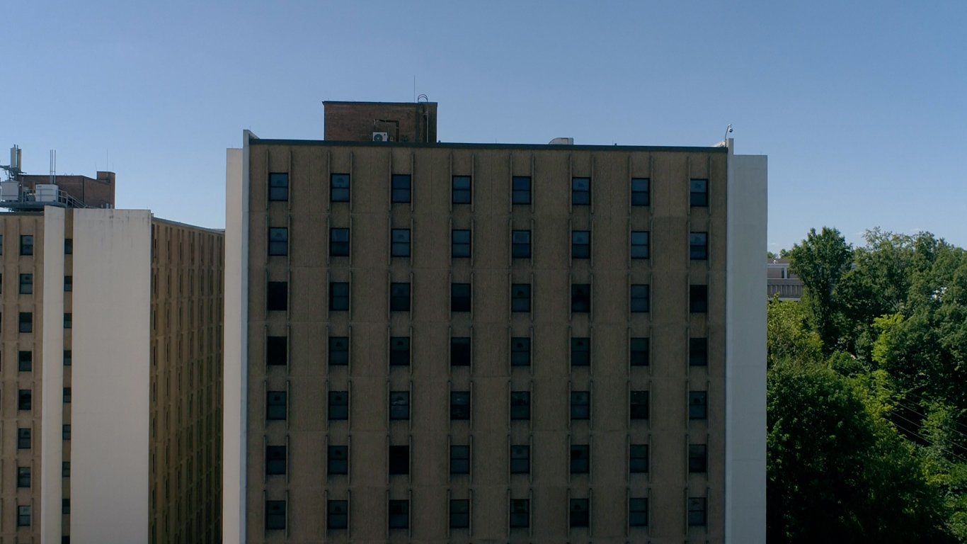 A large building with a lot of windows is surrounded by trees and a blue sky.
