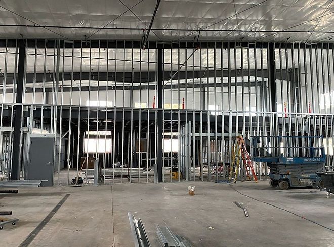 Interior view of a commercial building under construction. Metal framing defines interior walls, with a scissor lift and ladder present.