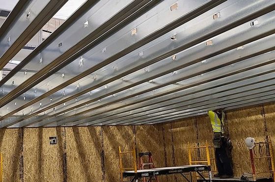 Metal ceiling framing being installed indoors; a worker stands on a scaffold.