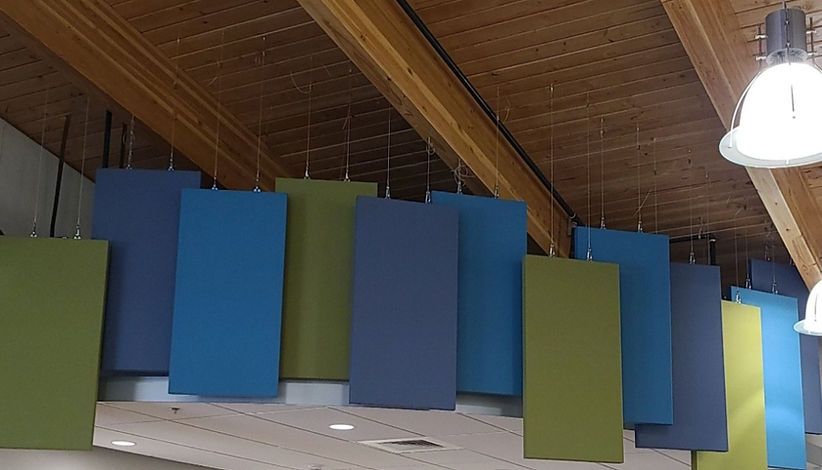 Colorful rectangular sound-dampening panels hanging from a wooden ceiling. Panels are blue, green, and grey.
