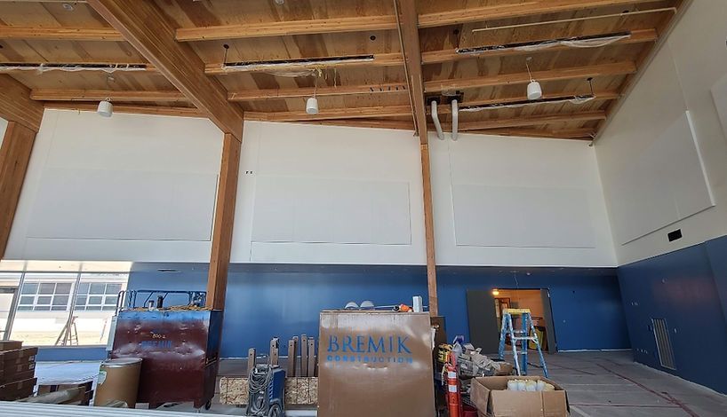 Interior view of a room under construction with exposed wooden beams, white walls, and blue lower walls. Construction materials are scattered throughout.