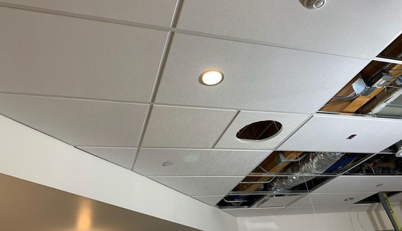 Acoustic ceiling tiles, some intact, others missing, reveal the space above, with a recessed light and a large hole.