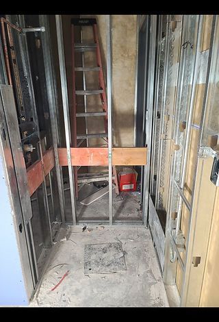 Interior construction framing a narrow vertical space. A ladder is set within the metal framework. Red electrical boxes are visible.