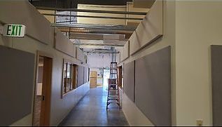 Hallway under construction, with gray acoustic panels on walls, exit sign, and a ladder.