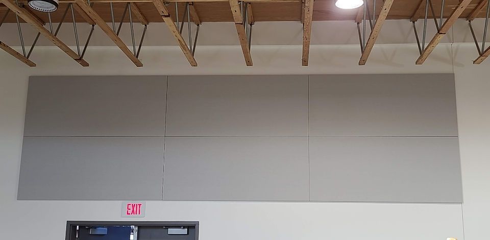 A room's ceiling with exposed wooden beams, a gray wall with three panels, and an 