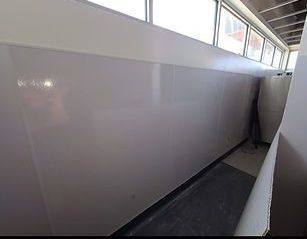 A narrow, light-walled corridor with a row of windows above. The floor is a mix of dark and light gray.