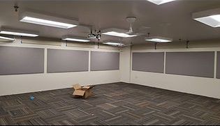 Empty classroom with grey acoustic panels, fluorescent lights, and patterned carpet. A cardboard box sits on the floor.