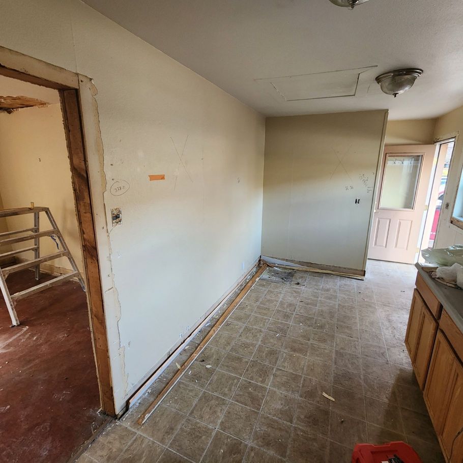 A kitchen undergoing renovation. Beige walls, linoleum flooring, and exposed doorways lead to other rooms.