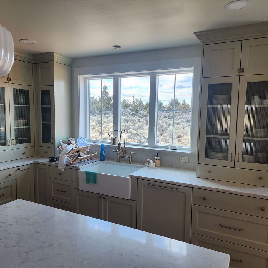 A bright kitchen with light-colored cabinetry, a farmhouse sink, and a large window overlooking a natural landscape.