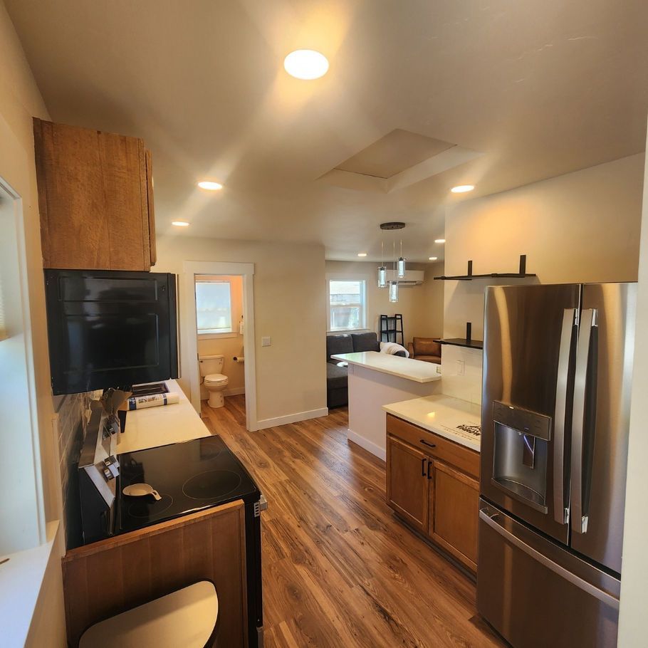 Kitchen with wooden floors, stainless steel refrigerator, and a white countertop. A bathroom is visible in the background.