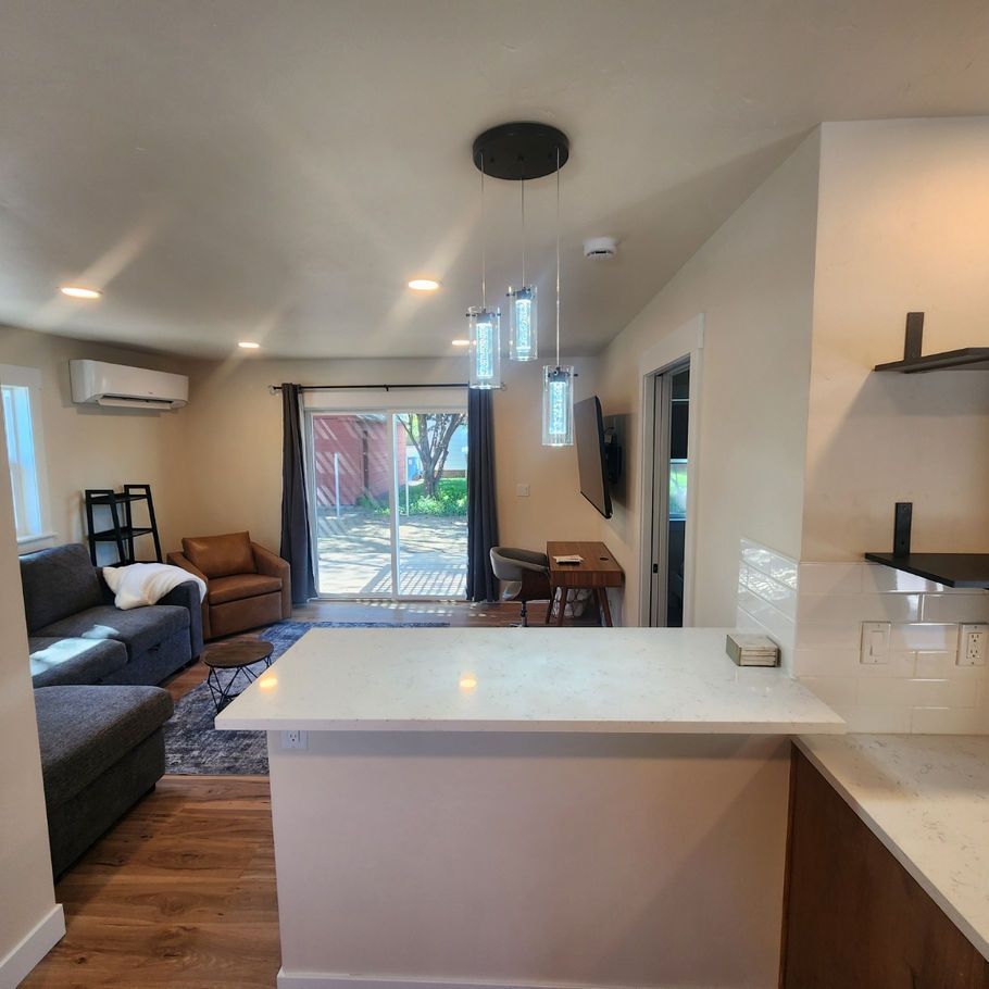 A modern living space with a kitchen island, sofa, and sliding glass door leading to a yard. Neutral tones dominate the space.