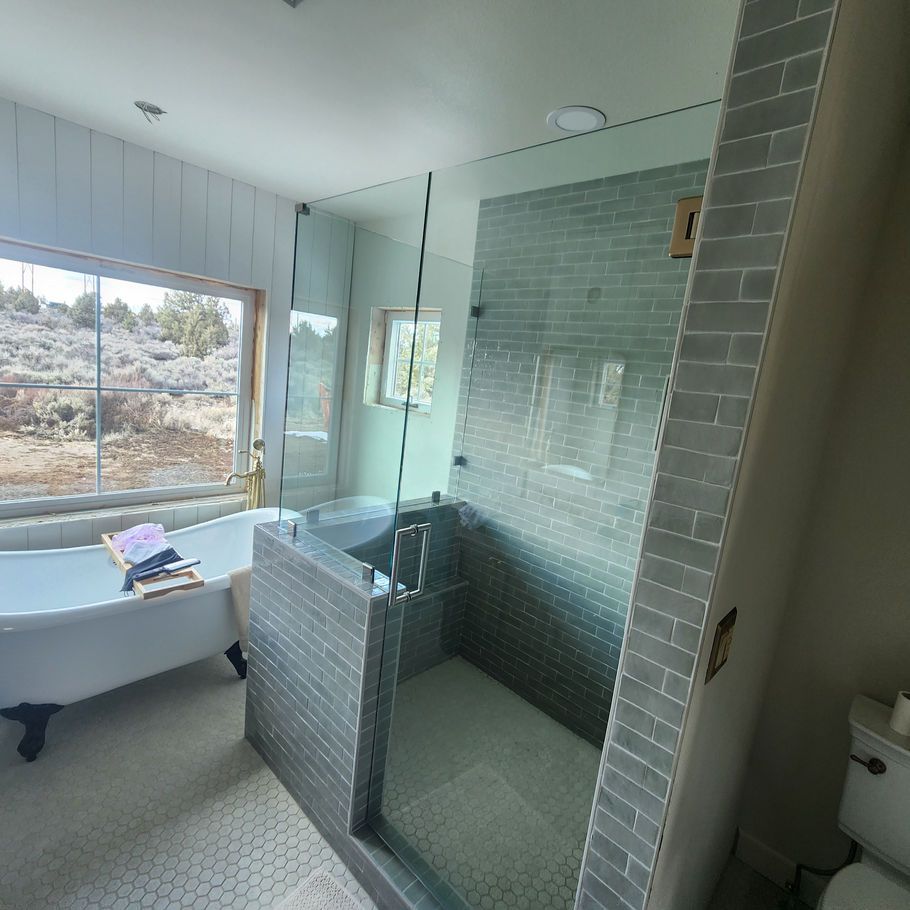 Spacious bathroom with a clawfoot tub by a large window, a glass shower, and light gray tiled walls.