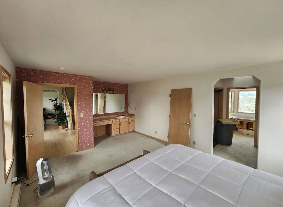 Bedroom with a bed, vanity, and doorways leading to other rooms. Walls have pink wallpaper and white paint.