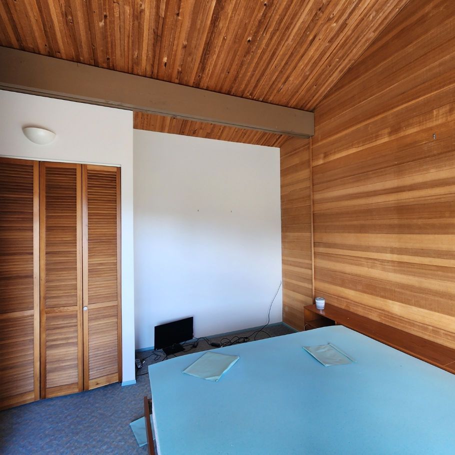 Bedroom with wood-paneled walls and ceiling, light blue bed, and a white wall for a TV.