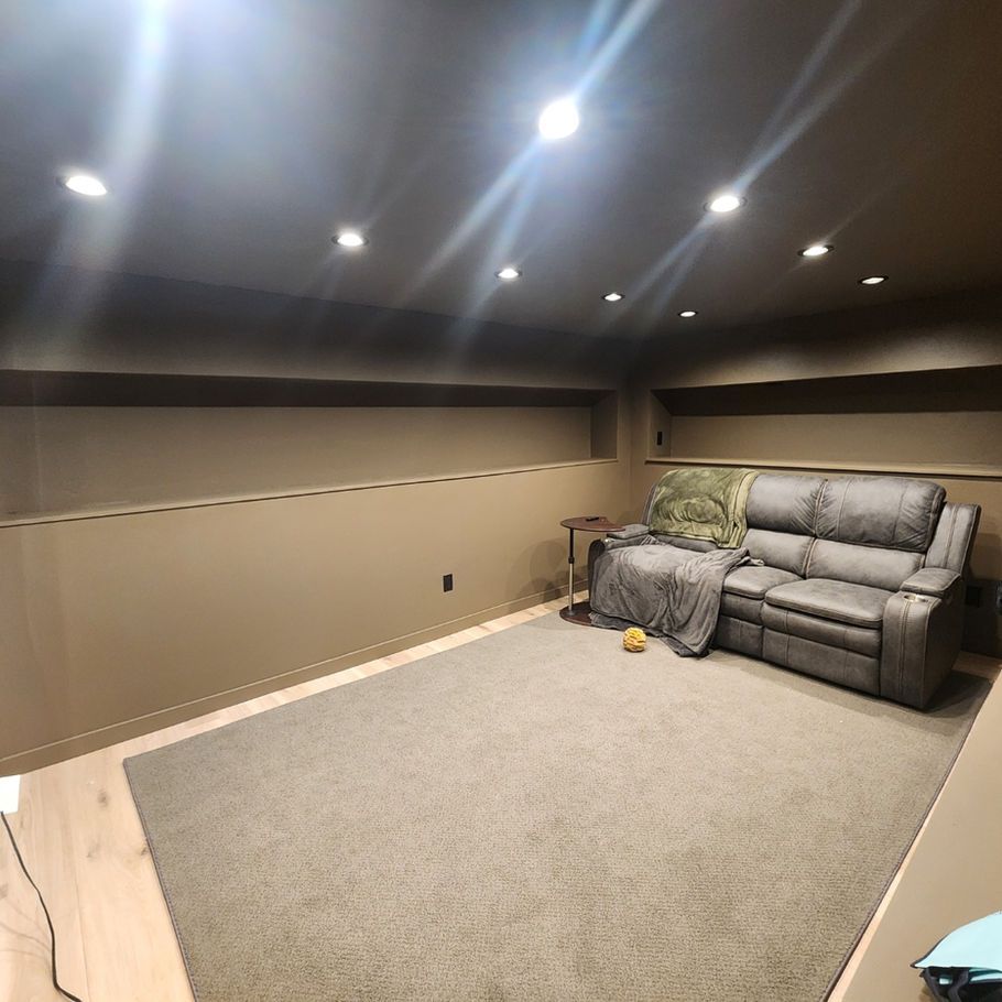 A basement living room with a gray sofa, beige walls, recessed lighting, and a gray carpet.