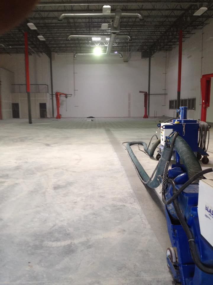A blue machine is sitting in the middle of a large empty warehouse.