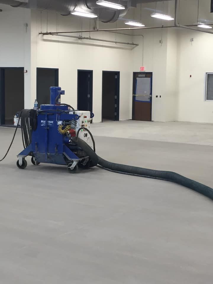 A blue machine is sitting in an empty room with a hose attached to it.