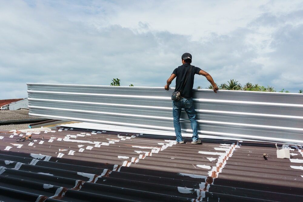 A Man is Standing on Top of a Roof Holding a Piece of Metal — Wagga Roof Repairs In Griffith, NSW