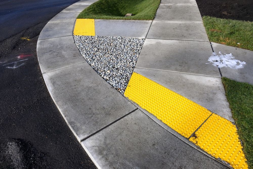 Curved curb with yellow tactile paving for the visually impaired and a triangular gravel area for drainage.