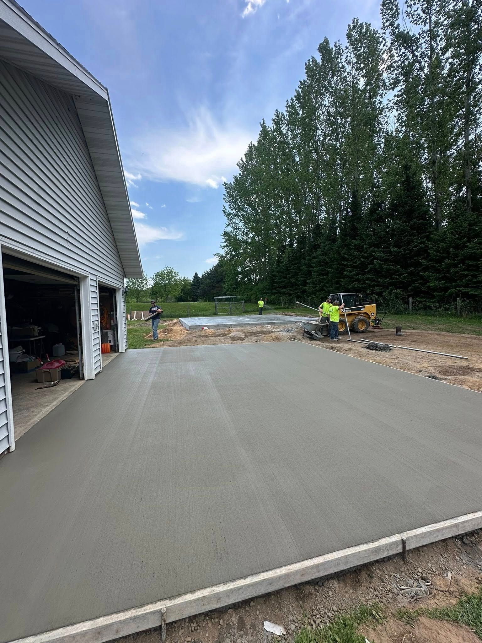 New concrete driveway next to a gray house, with construction workers and equipment in the background.