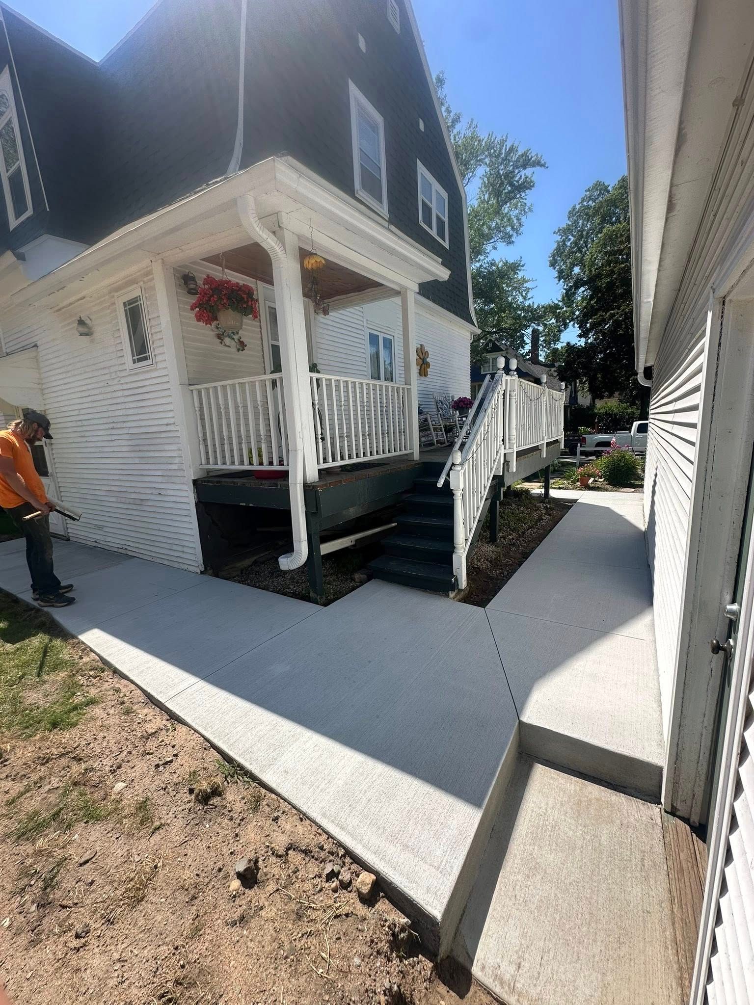 A house with a white porch and deck, concrete walkway, and a worker in orange.