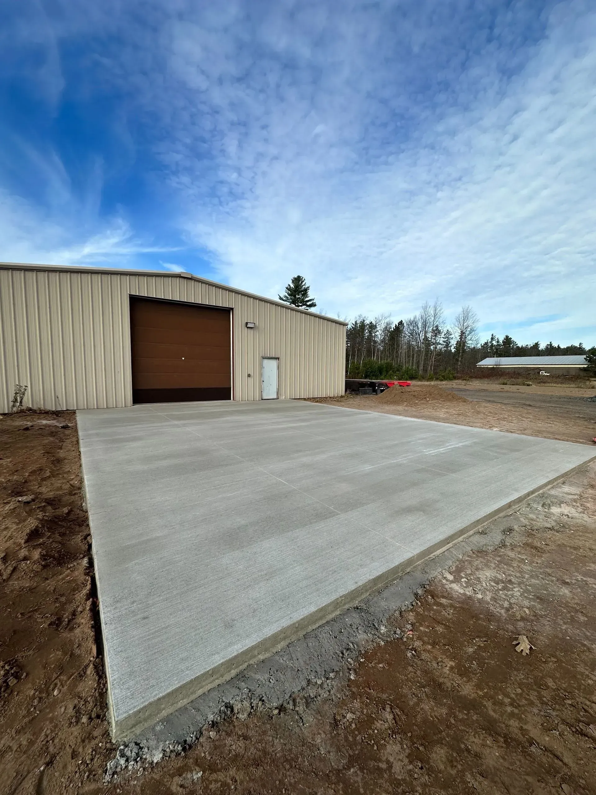 Newly poured concrete slab in front of a metal warehouse building, against a blue sky.