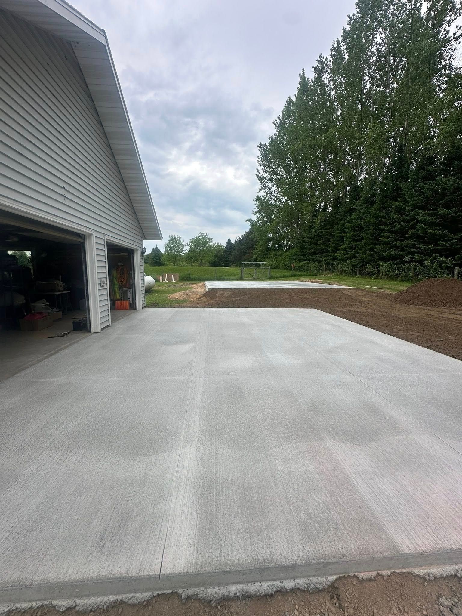 New concrete driveway next to a white garage with open doors; overcast sky.