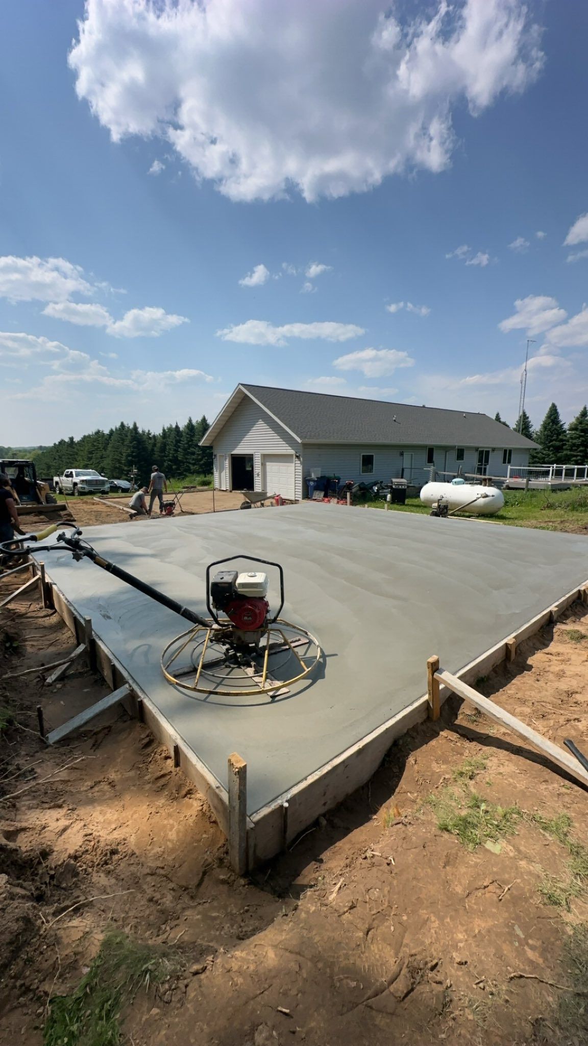 Freshly poured concrete slab being smoothed with a power trowel; a building is in the background.