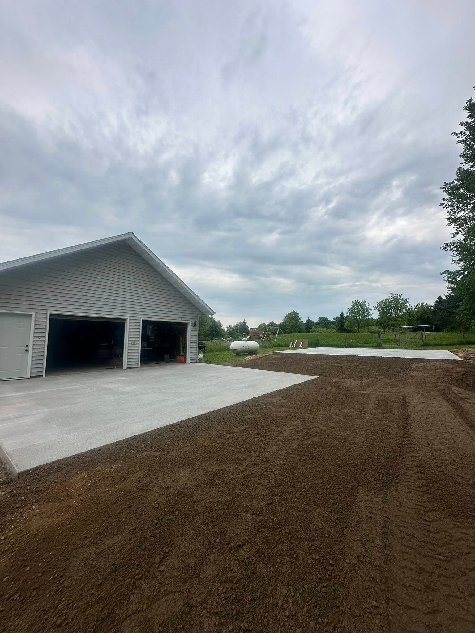 New concrete driveway with a two-door garage under a cloudy sky. Gravel foreground.