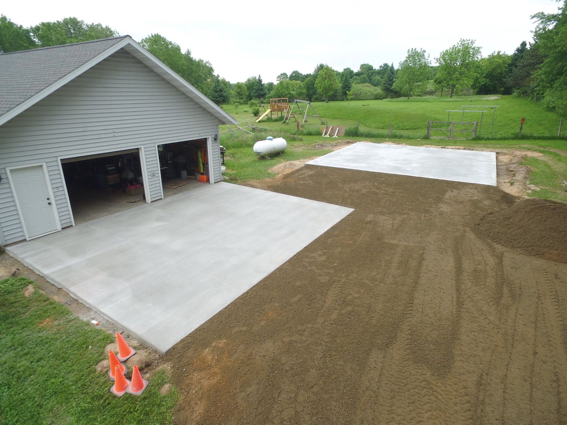 New concrete garage pad and driveway with freshly laid dirt and surrounding grassy yard.