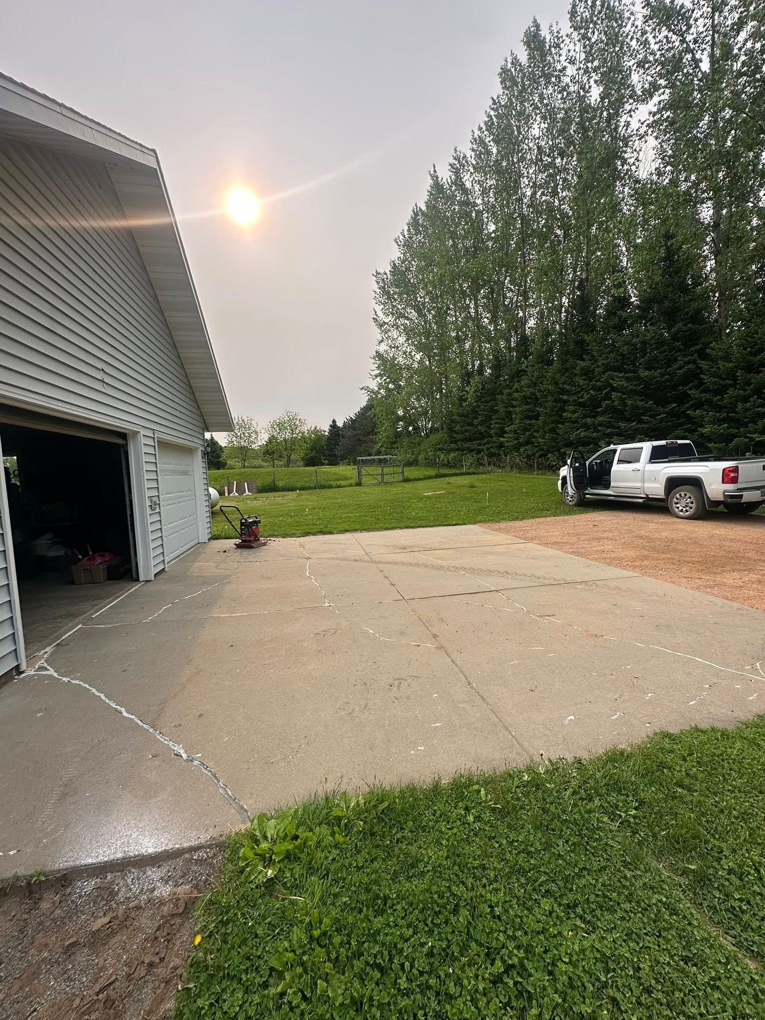 Concrete driveway next to a white garage, a white pickup truck, and green grass. Bright sun in the sky.