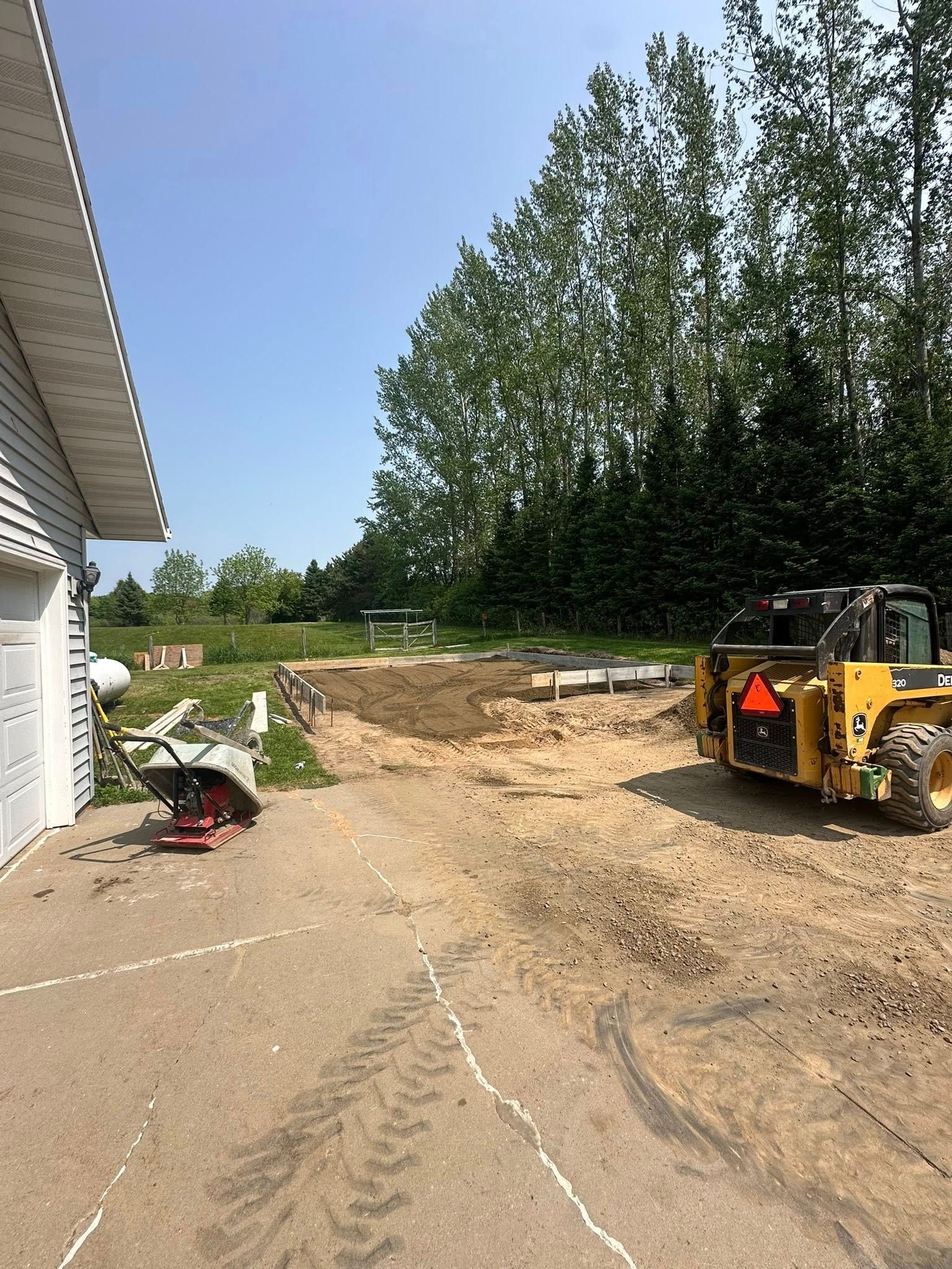 Construction site with a skid steer, cleared ground, and a building on a sunny day.