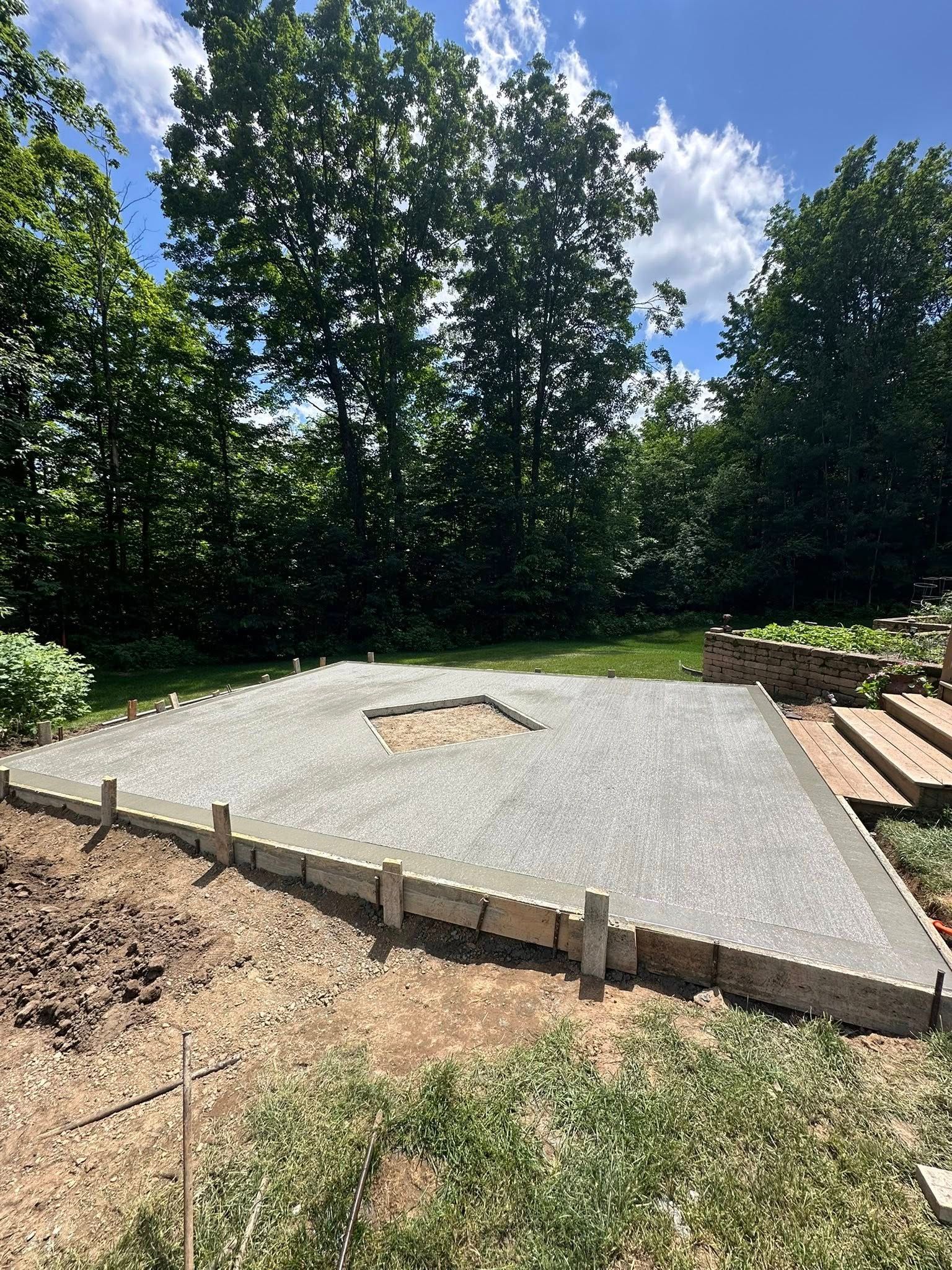 Newly poured concrete slab in a yard, framed by wooden forms, with trees in the background.