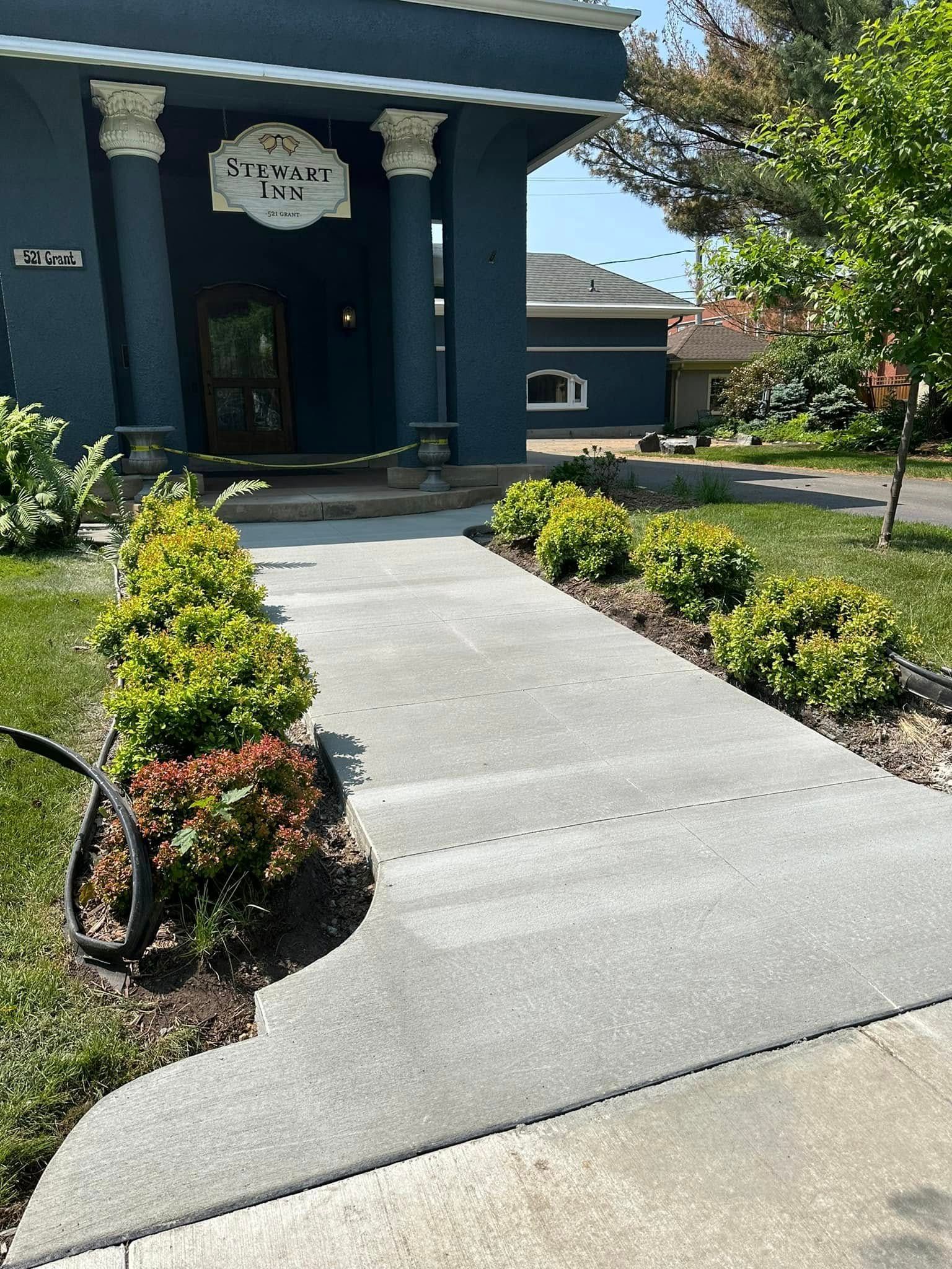 Blue building with white columns, concrete walkway, and green bushes.