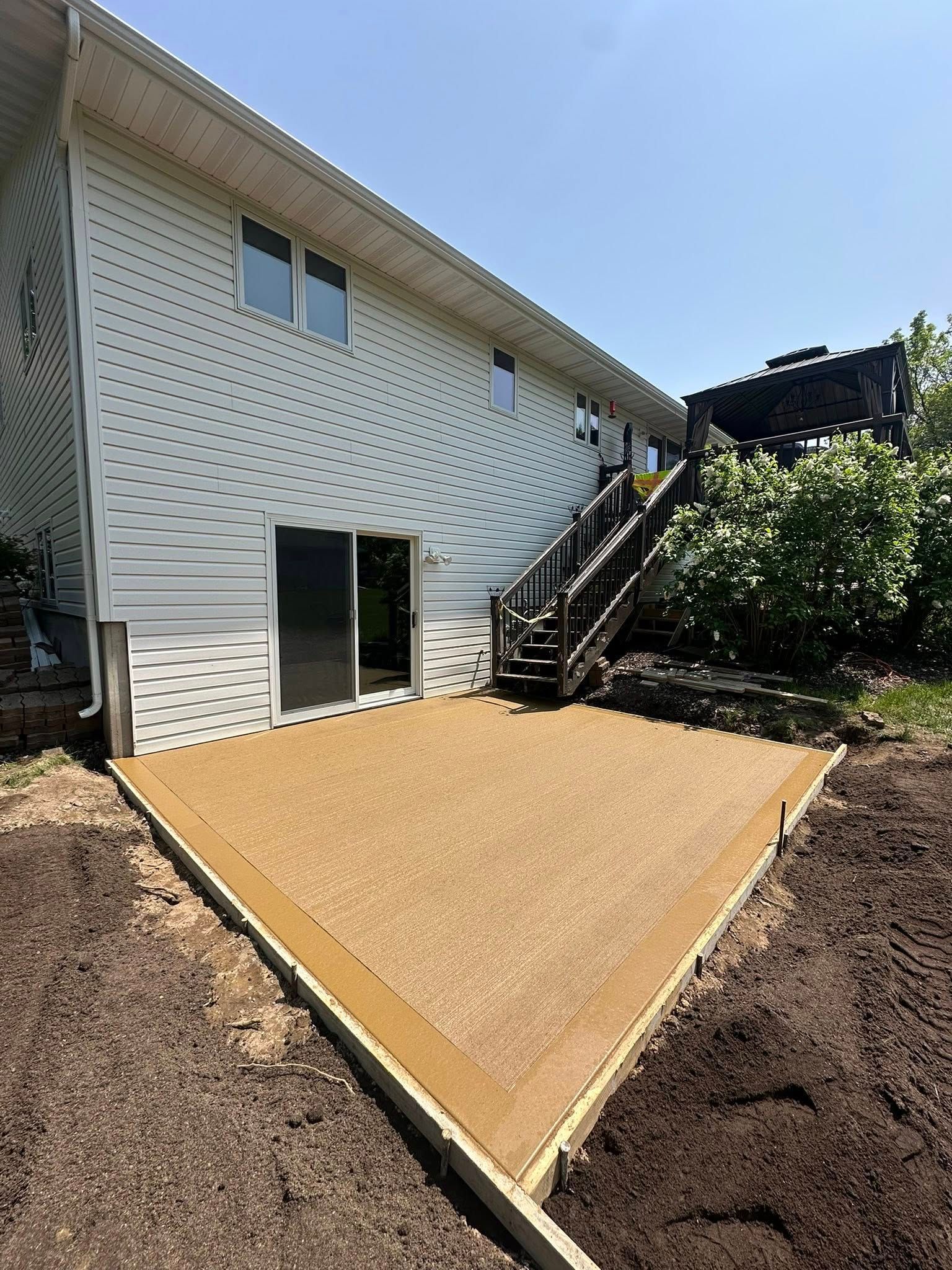 A newly built, brown composite deck next to a two-story white house with a sliding glass door and wooden stairs.