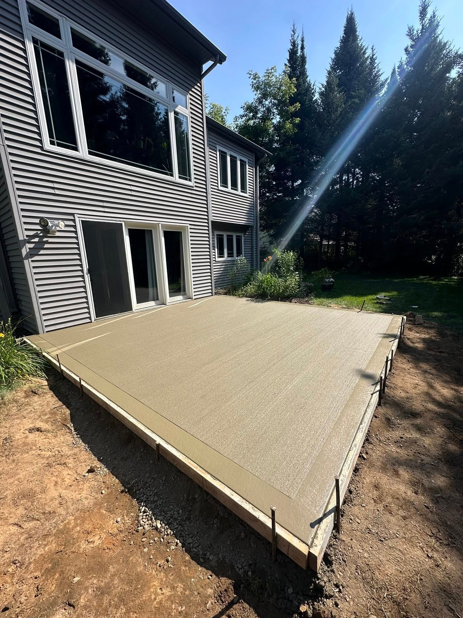 Newly poured concrete patio next to a two-story house with large windows.