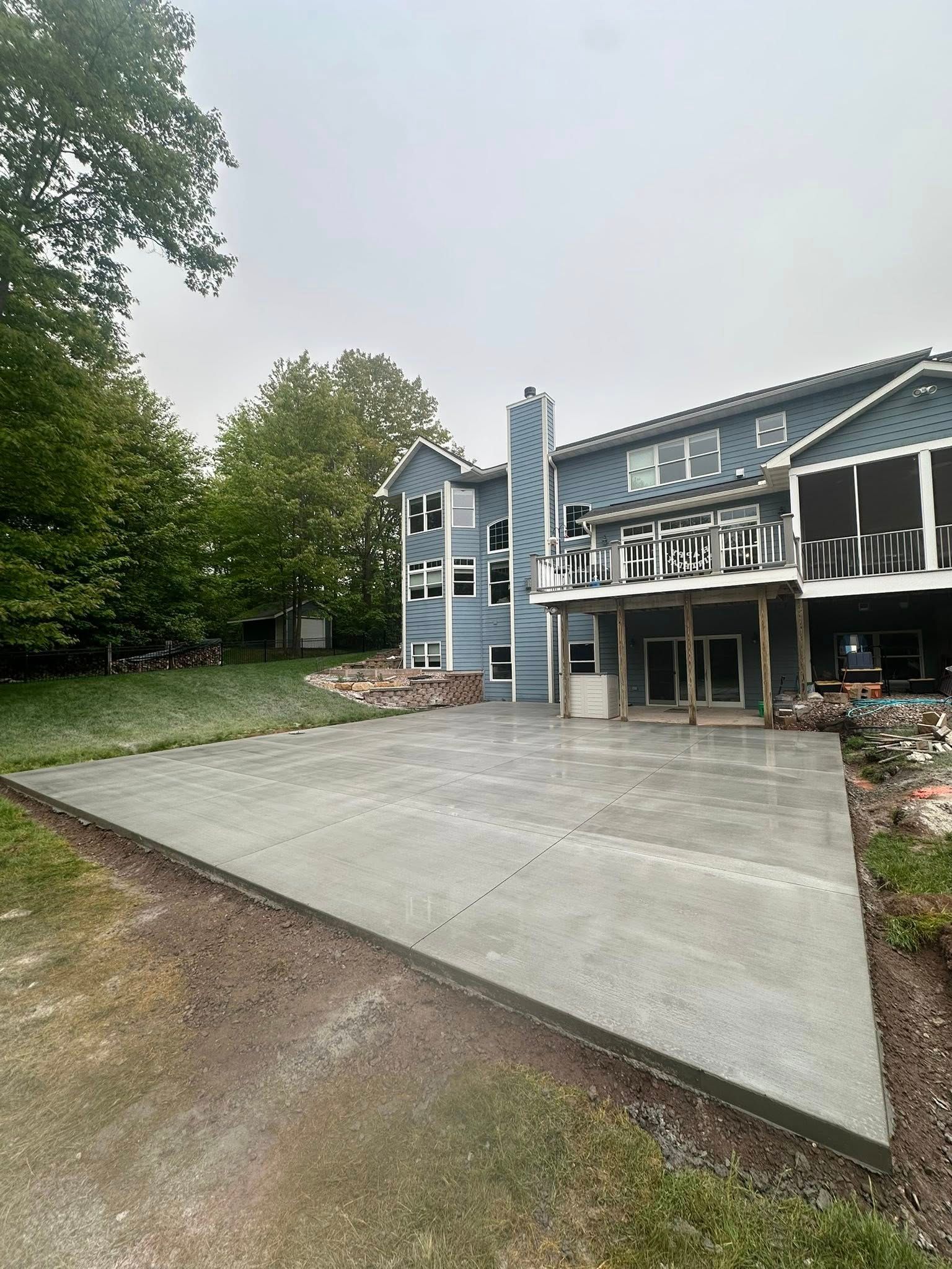 Newly poured concrete patio next to a light blue house with a deck.