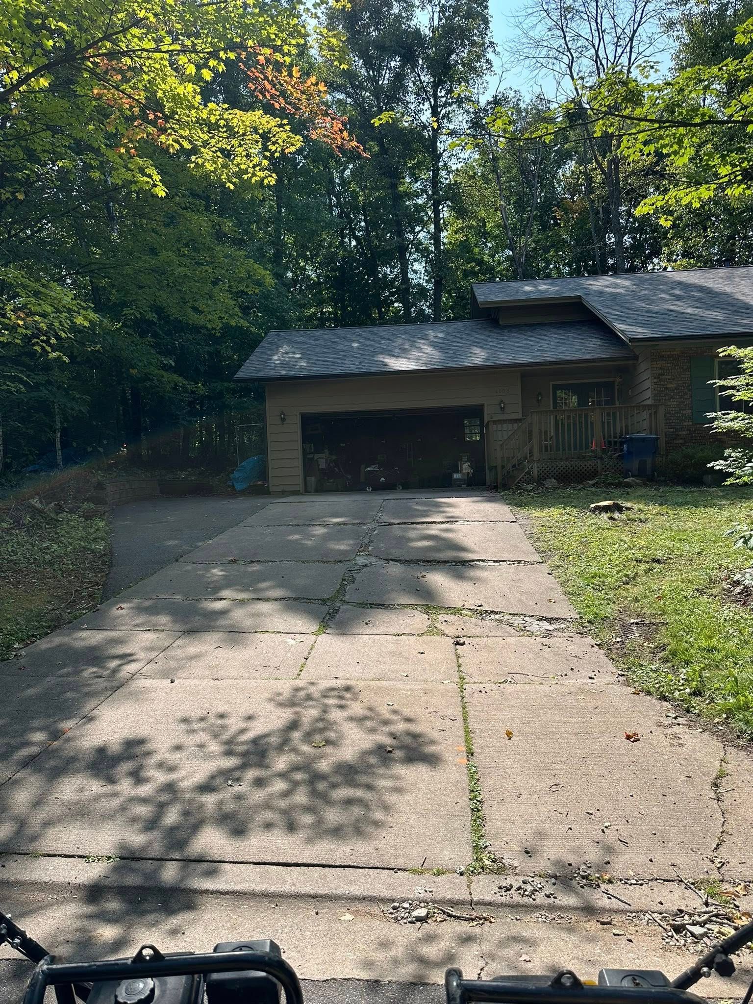 Driveway leading to a one-story house with a garage, trees in the background, sunny day.