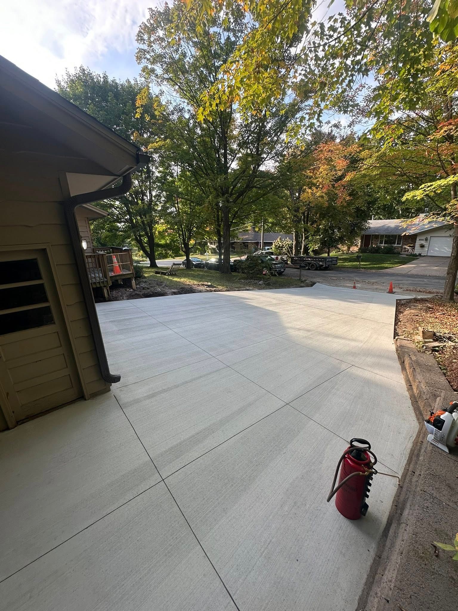 Concrete driveway next to a tan house, spray bottle on the side, trees in the background.